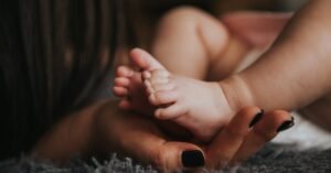 maternal nutrition Close-up of a mother's hand gently holding her baby's tiny feet, symbolizing warmth and affection.